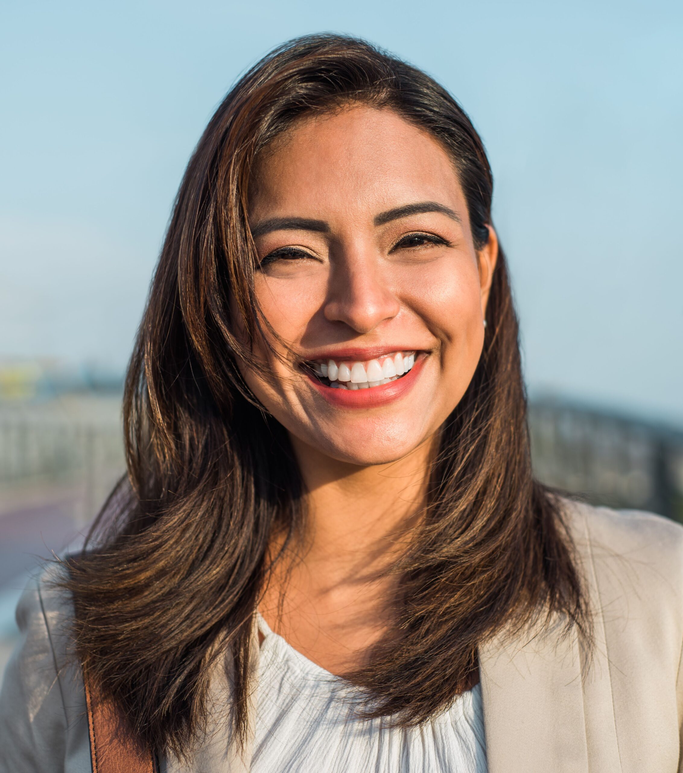 Mujer sonriente mostrando una sonrisa saludable y natural, con el cabello castaño al viento en un entorno exterior luminoso, representando el resultado ideal del tratamiento con los dentistas en Valladolid de la clínica MYM