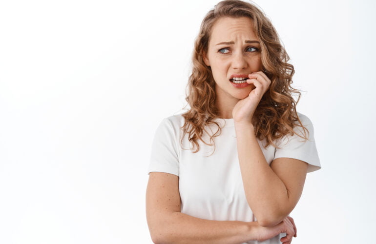 Mujer joven con expresión de dolor tocándose la mejilla derecha por muelas picadas y dolor intenso, pensando en visitar ak dentista en la clínica dental MYM