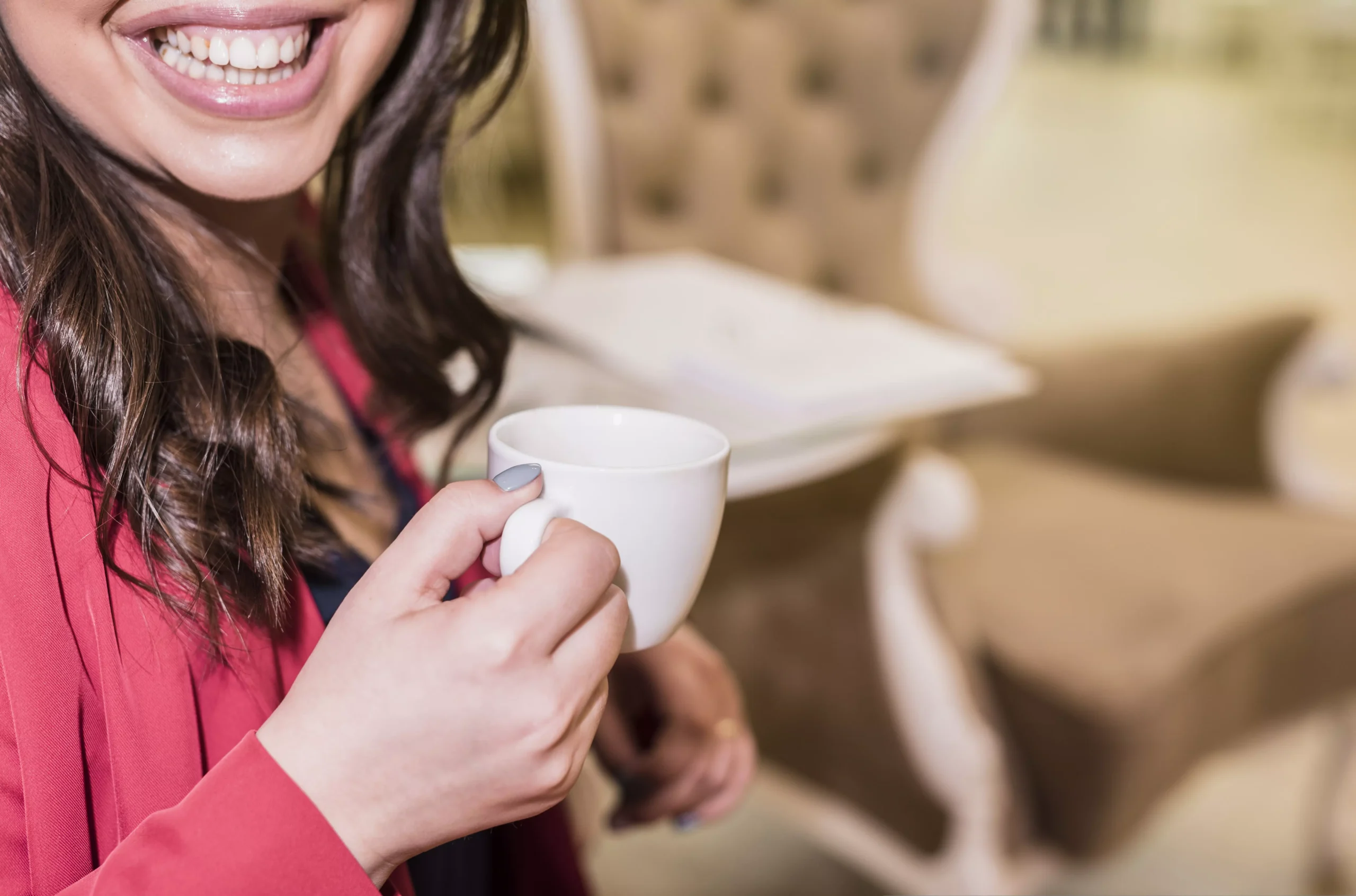 Mujer sonriendo con dientes blancos mientras sostiene una taza de café, en referencia a las posibles manchas en los dientes por el consumo de bebidas como el café.